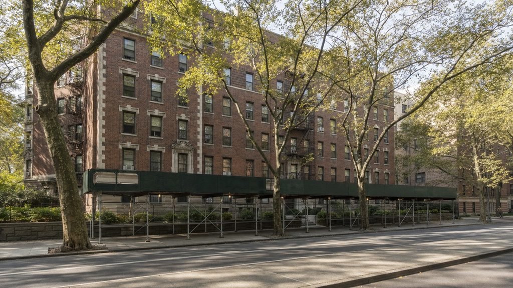 Seven-storey brick apartment building on a tree-lined Brooklyn parkway behind a sidewalk shed