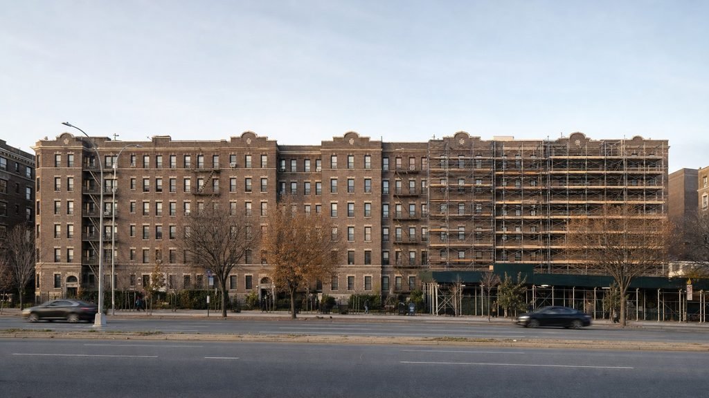 Six-storey brick apartment block on Queens Boulevard, partly scaffolded with a sidewalk shed